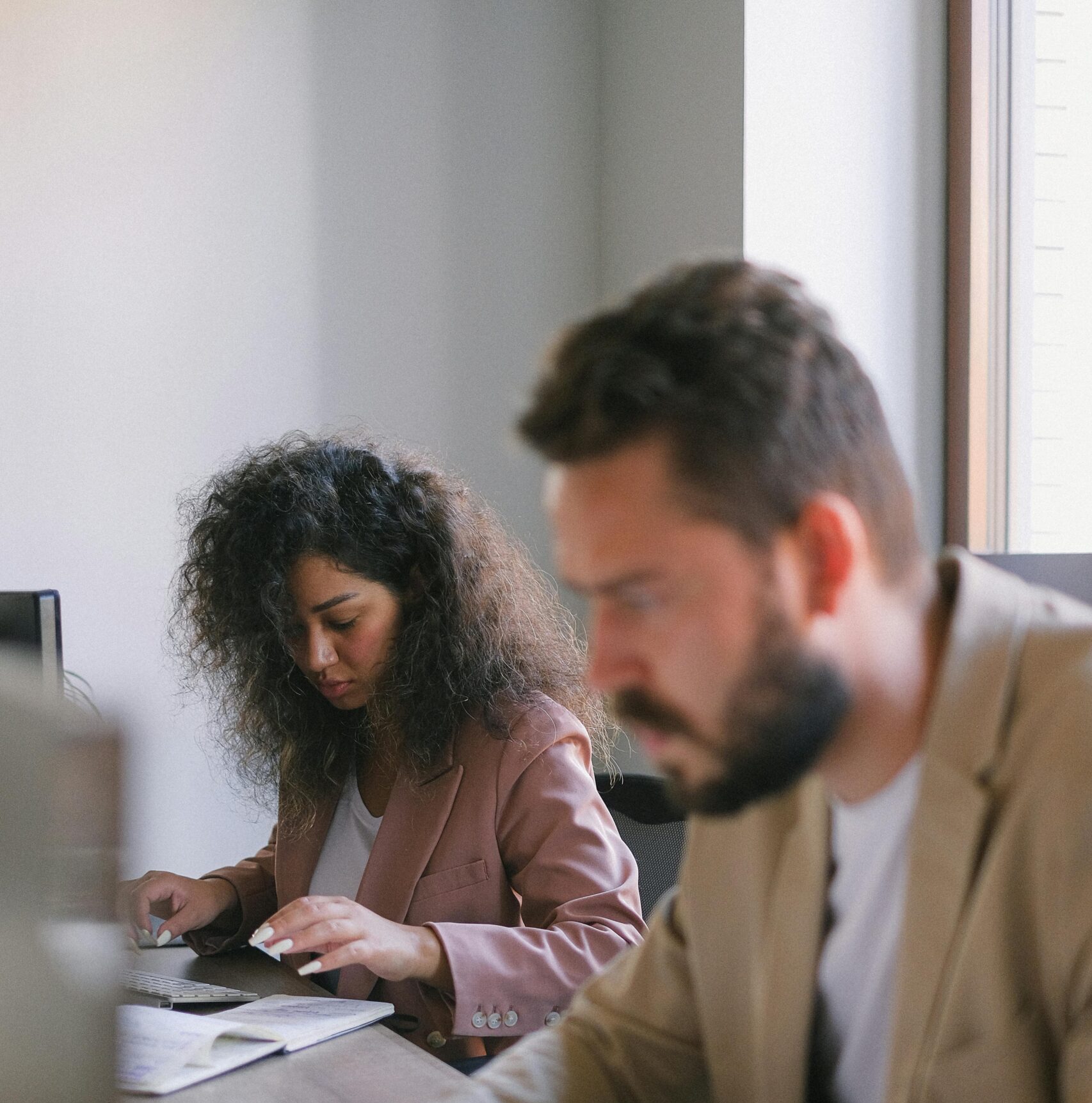 Blurred man and woman typing on computers and sitting at table while working together in modern office